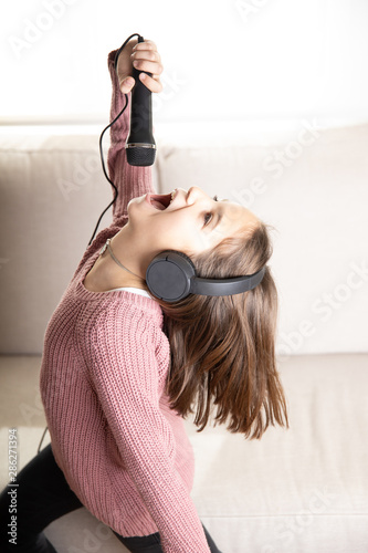 Konstfotografi Niña cantando feliz con auriculares y micrófono en interior de casa