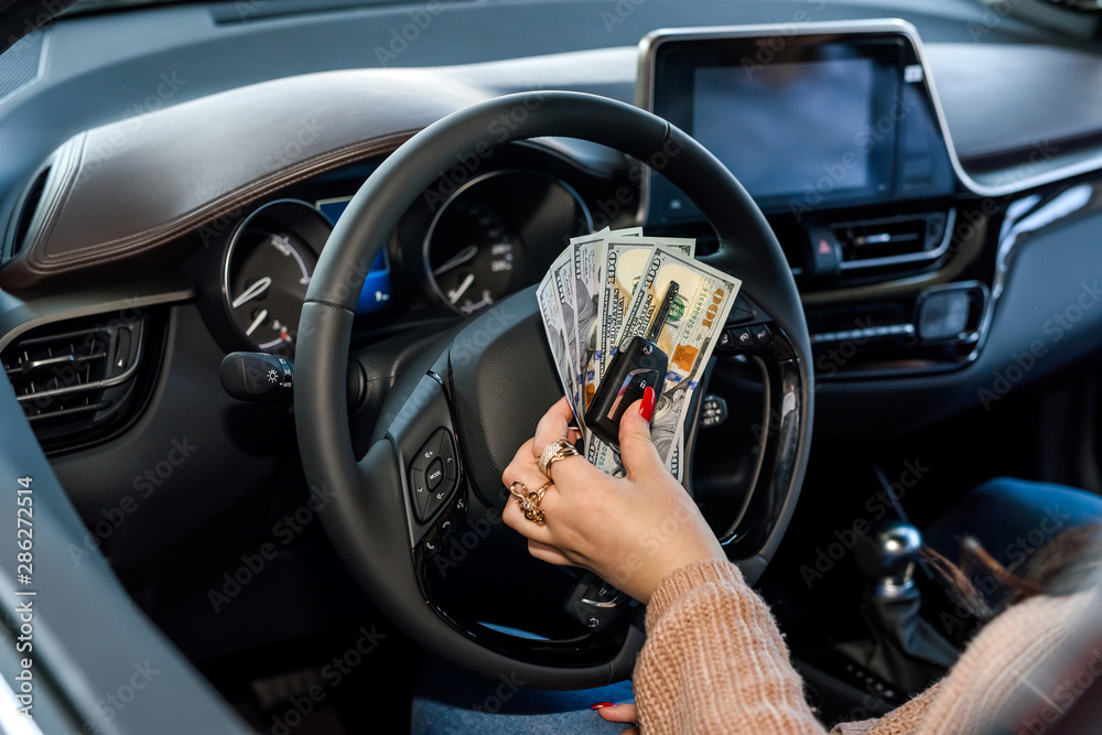 Woman sitting in new car and showing dollars and keys