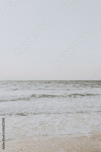 Beautiful tropical beach view with white sand and beige sea with waves on Phuket, Thailand. Minimal composition with neutral colors. Summer concept. Natural background.
