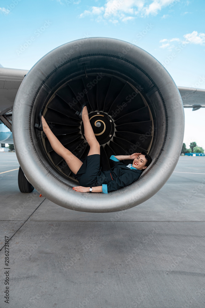 Laughing Caucasian woman in uniform lying in airplane turbine outdoors