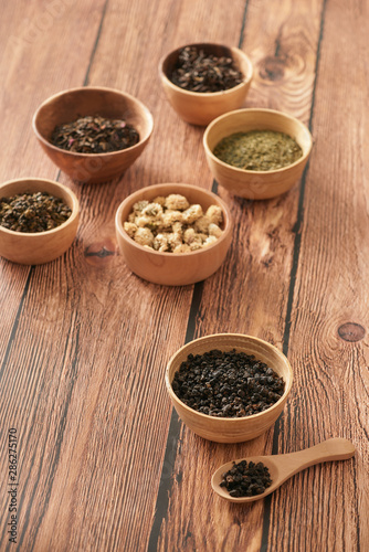 assortment of dry tea in white bowls on wooden surface