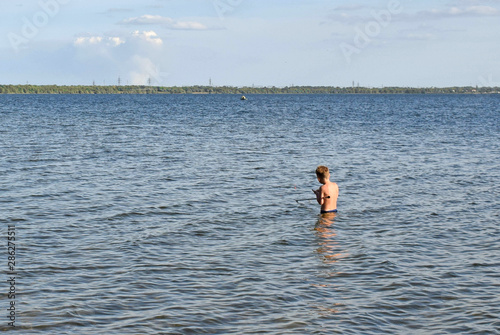 Young boy with a home fishing rod. Fishing in the lake on a summer day. Little fisherman is fishing. Boy learns to fish.