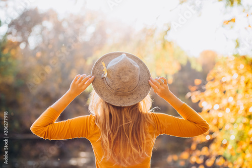 blonde in a yellow jacket on a background of autumn nature. the frame is lit by sunlight. A young woman in a gray hat looks at the autumn forest. Portrait of a woman in autumn