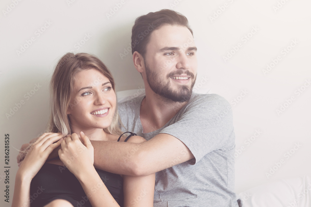 Couple in bed. Young white male and blonde female. Sitting in bed with happy smile. Modern couple lifestyle concept. With light leak. Couple in bed. Young white male and blonde female. Sitting in bed with happy smile. Modern couple lifestyle concept. With light leak.