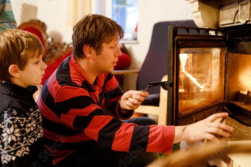 Middle age father sitting by fireplace with little kid boy at home. Happy family, dad with son make fire for Christmas time. Safe handling for kids photo