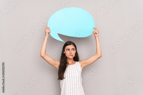 Image of displeased brunette woman wearing dress frowning and holding blue copyspace thought bubble