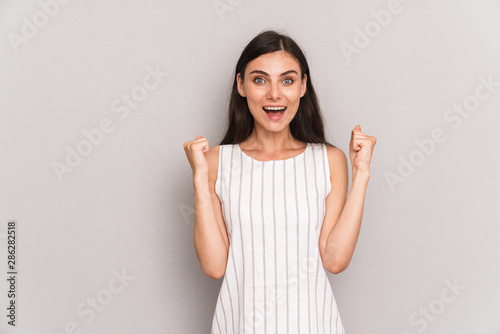 Image of positive brunette woman wearing dress smiling and doing winner gesture