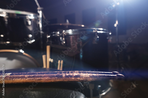 Close-up of used drumsticks lie on a drummer's chair against the background of a drum kit and flare of spotlights. The concept of music