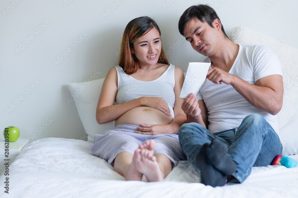 Pregnant woman in bed with man. Asian woman with white man. Holding xray photo. Mix race relationship concept. Talking about their lives. Pregnant woman in bed with man. Asian woman with white man. Holding xray photo. Mix race relationship concept. Talking about their lives.