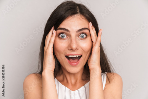 Image closeup of cheerful woman with long dark hair expressing surprise and touching her cheeks