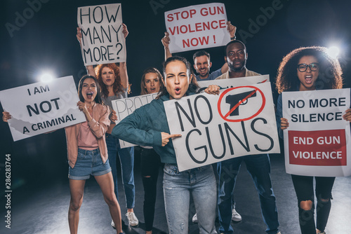 emotional girl pointing with finger at placard with no guns lettering near multicultural people on black © LIGHTFIELD STUDIOS
