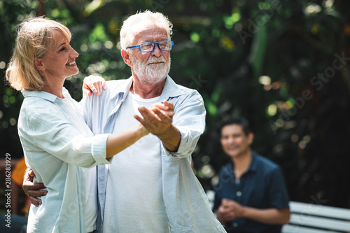 senior couple dancing outdoor. White male and female with tropical garden background. Happy smile. Hair light. Happy retirement concept.