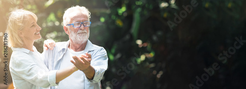 senior couple dancing outdoor. White male and female with tropical garden background. Hair light and light leaks. Happy retirement concept. Banner frame.