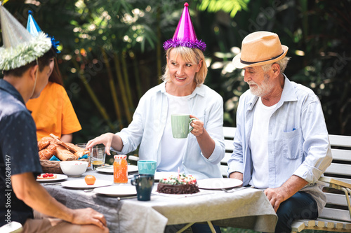 Senior birthday in. backyard tropical garden. White  asian senior man and woman with young couple. Enjoying a birthday party at home garden. Talking and smile.