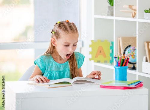 Cute girl reading books at schooldesk