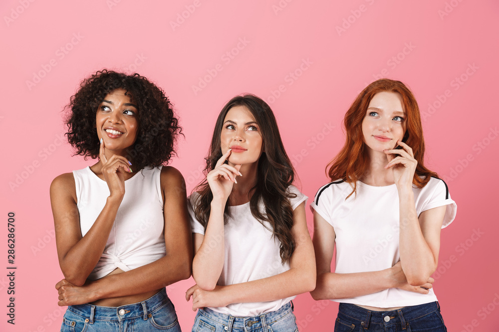 Thinking thoughtful cute multi-ethnic girls friends posing isolated over pink wall background. - obrazy, fototapety, plakaty 