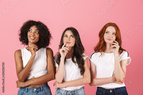 Thinking thoughtful cute multi-ethnic girls friends posing isolated over pink wall background.
