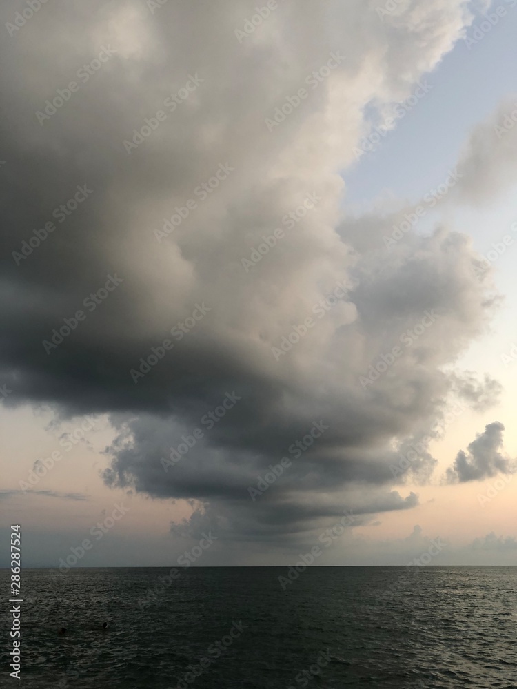 Thundercloud over the sea at sunset. A dark cloud against the blue sky, the sun disappeared beyond the horizon. Summer evening on the beach, beautiful sky.