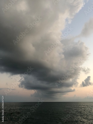 Thundercloud over the sea at sunset. A dark cloud against the blue sky, the sun disappeared beyond the horizon. Summer evening on the beach, beautiful sky.
