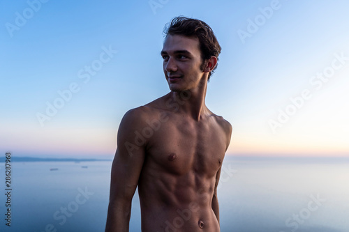 Portrait of a young beautiful male model outdoors by the sea at sunset