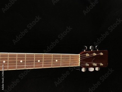 Part of an acoustic guitar on a black background. Six-string guitar, light wood color. String musical instrument. Classical guitar, close-up.