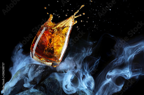 Glass of whiskey .Splash.Creative photo glass of whiskey on stone with fog and black background.Copy space.Advertising shot