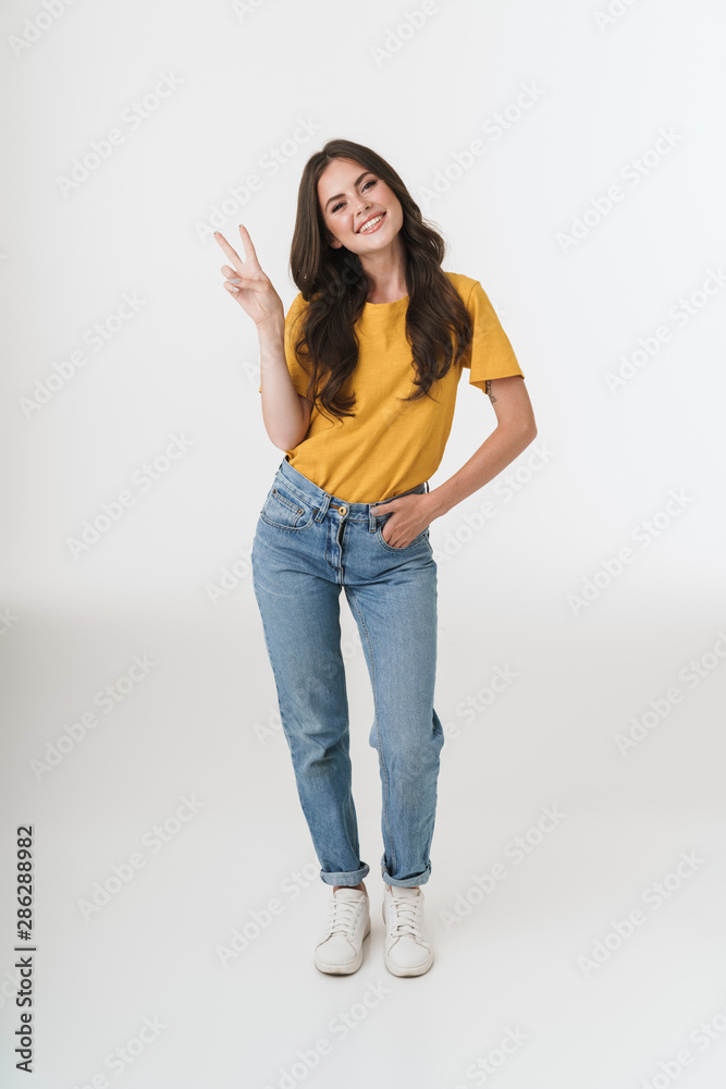Full length image of gorgeous brunette woman wearing casual clothes smiling  and showing peace sign Stock Photo