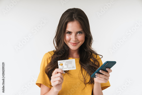 Image of charming brunette woman wearing casual clothes holding credit card and cellphone