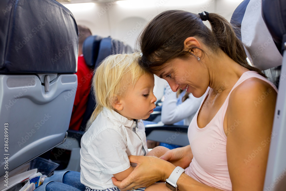 Mother and son, toddler boy, sitting together in airplane furing flight for a family holiday