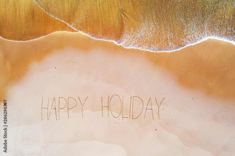 Fototapeta premium Aerial top shot from ocean waves and handwritten Happy holiday at the beach