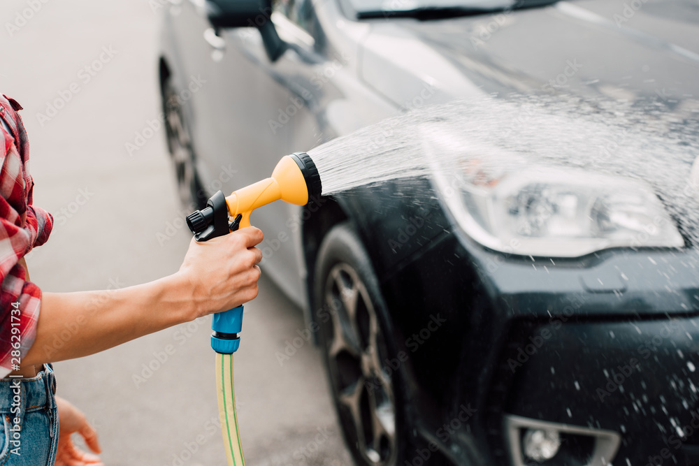 cropped view of woman washing black car while holding pressure washer