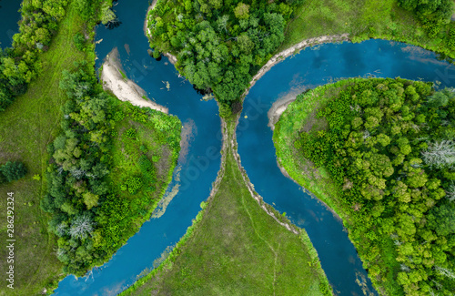 Top view drone shot of a green field, forest and river