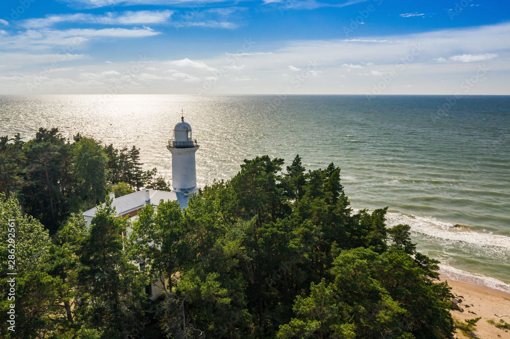 View of the sea and the Uzhava lighthouse in Latvia. Blue sky. Green forest.