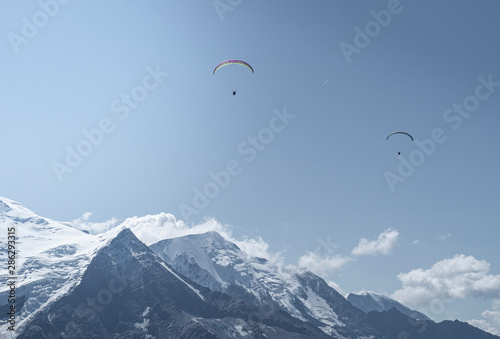 Two Parachouttes going side to side in the blue sky with clouds in the French Alps, Chamonix during a summer tour, fly and sport.