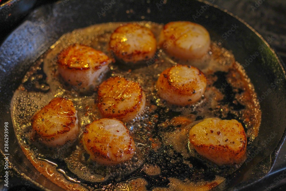 Selective Focus closeup of perfectly seared fresh sea scallops in butter and cracked pepper, sizzling on a cast iron skillet Selective Focus closeup of perfectly seared fresh sea scallops in butter and cracked pepper, sizzling on a cast iron skillet