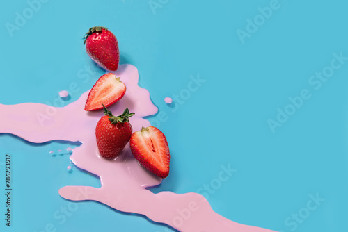 Red strawberry laying on blue background. Pink yogurt. Food idea concept. Bright colors