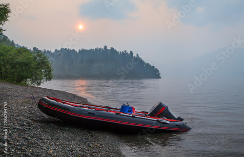 The boat on the lake, the sun on the sunset sky, fog. Water travel, summer vacation, fishing.