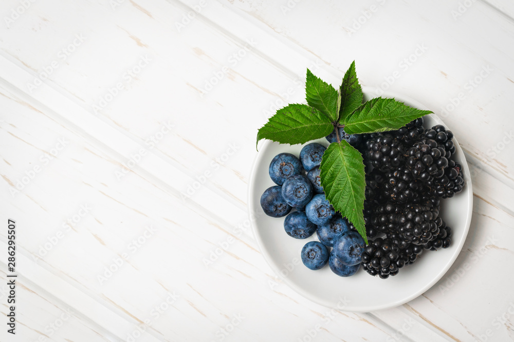 Top view ripe blackberries and blueberries in a white dish on a wooden table with copy space