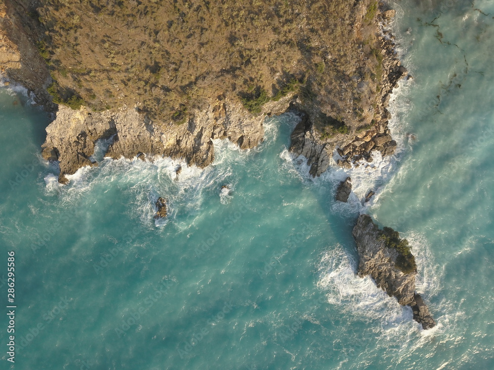 Aerial view of small beach with turquoise water next to rocks and trees in the area of Agia Paraskevi Halkidiki, Greece. View from drone