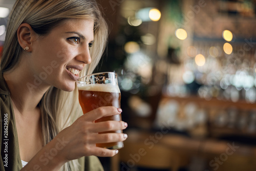 Close up of happy woman with glass of beer in a pub and looking away