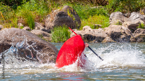 Playboating. A man sitting in a kayak with oars in his hands performs exercises on the water. Kayaking freestyle on whitewater. Eskimo roll.