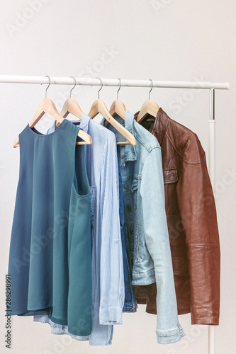 Collection of clothes hanging on rack near white wall. Clothes for women in blue colors. Office Style. © Natali Illar