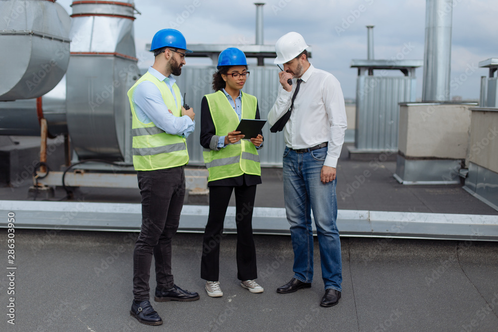 Good looking multiethnic group of workers in a modern building construction site analyzing the plan of construction they wearing the safety helmets Good looking multiethnic group of workers in a modern building construction site analyzing the plan of construction they wearing the safety helmets