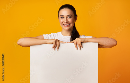 Smiling Girl Holding Empty White Board On Yellow Studio Background