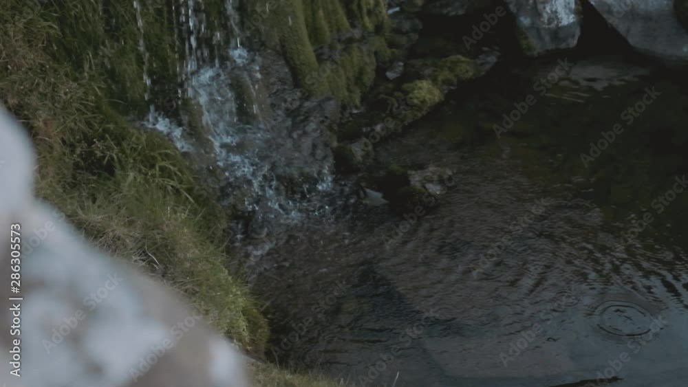 Tilt-down shot of a small waterfall pouring water into a stream Tilt-down shot of a small waterfall pouring water into a stream