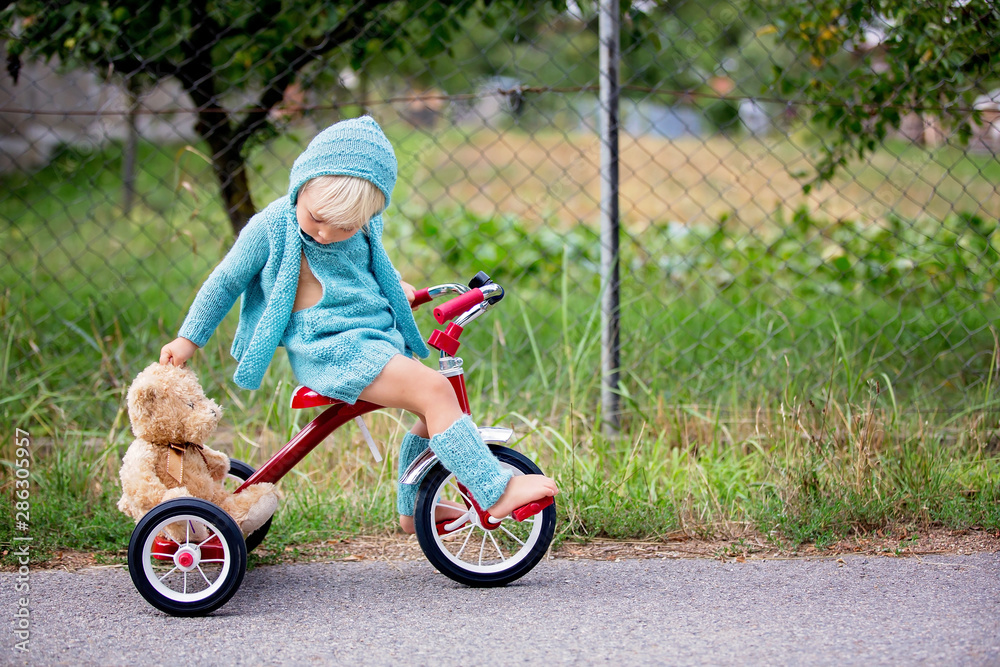 Adorable toddler boy with knitted outfit, riding tricycle on a quiet village street Adorable toddler boy with knitted outfit, riding tricycle on a quiet village street