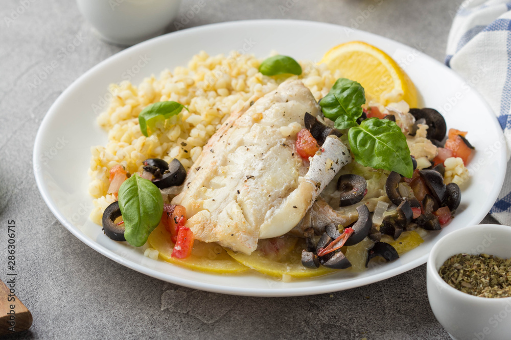 Baked white fish fillet (Pollock, cod, sea bass, Dorada) with olives, tomatoes and lemon. Traditional French food, bulgur Baked white fish fillet (Pollock, cod, sea bass, Dorada) with olives, tomatoes and lemon. Traditional French food, bulgur
