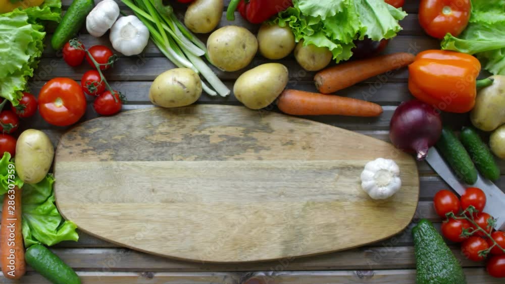Top view of hands of unrecognizable male cook sliding bulb of garlic on wooden cutting board with copy space while preparing food on kitchen table with lots of fresh vegetables around