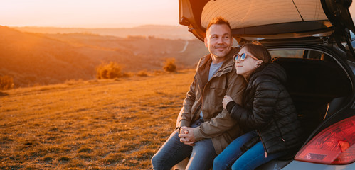 Daughter embracing father while sitting in a car trunk