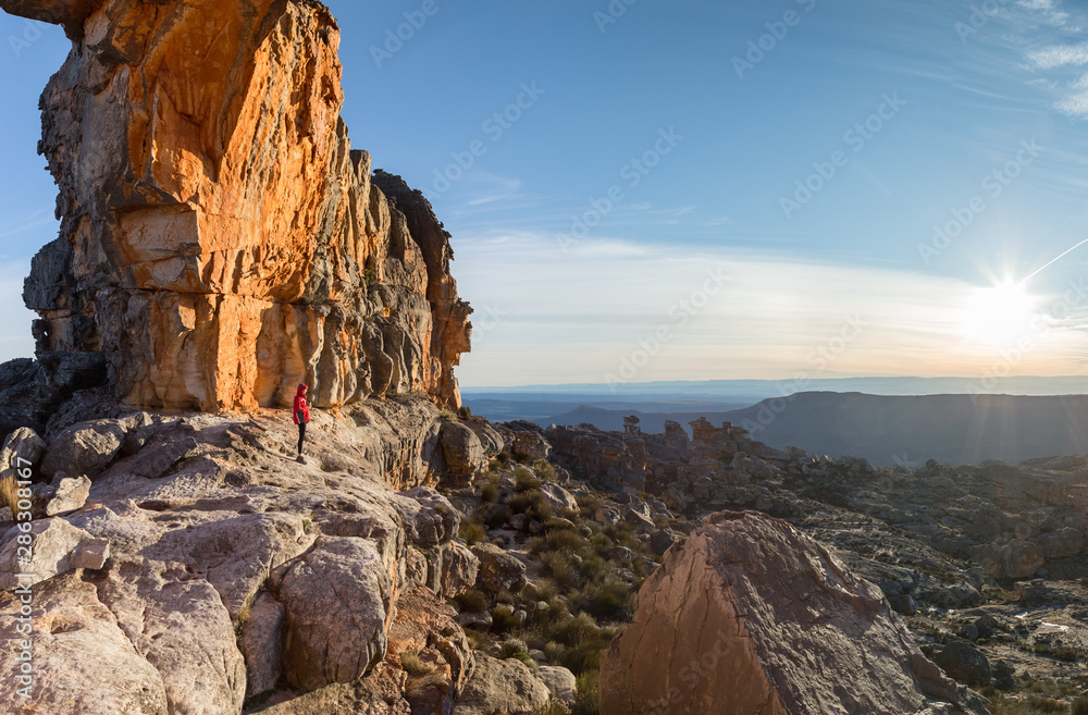 Hiker standing beneath rock formation at sunset